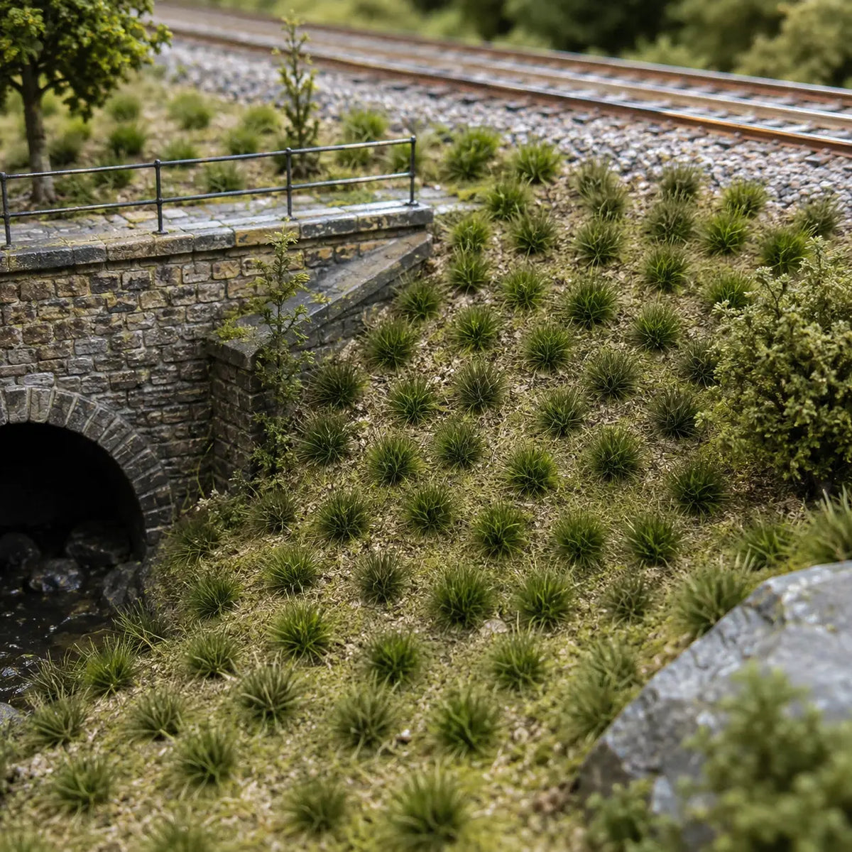 Realistic grass tufts covering a model railway embankment beside a stone tunnel