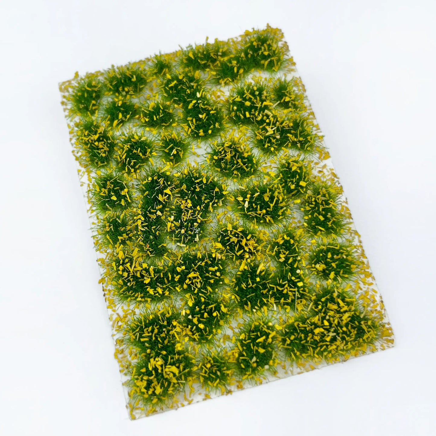 Closeup shot of peel-off self-adhesive deep green static grass tufts sheet, removable individual grass clumps with tweezers, realistic static grass mat miniature lawn terrain for scale model building, wargame tabletop base, railway layout scenery and diorama craft hobby supplies