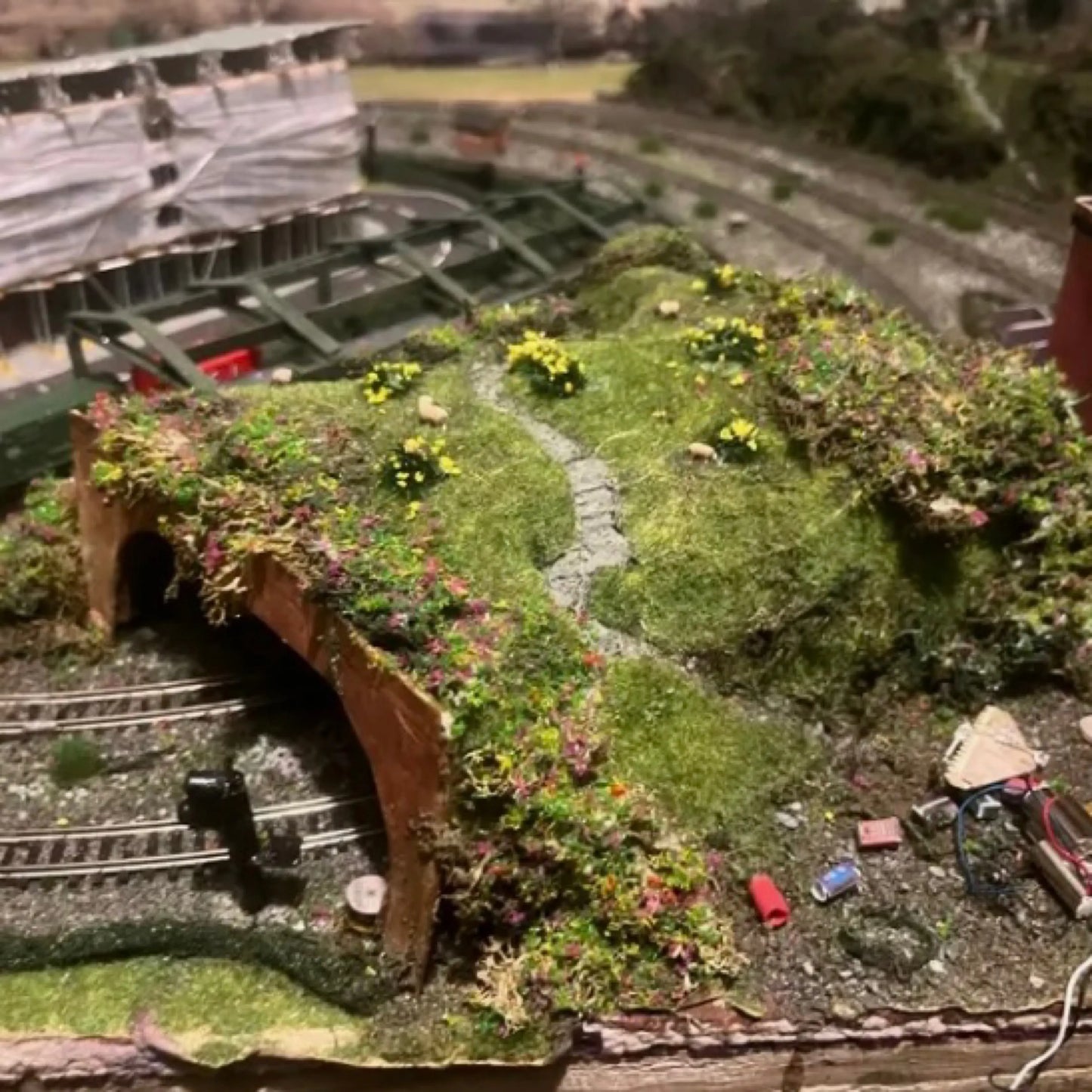 Realistic hillside railway tunnel diorama terrain covered with mixed seasonal self-adhesive tuft grass sheets, railroad landscape showcase for train scale model layout and hobby scenery creation
