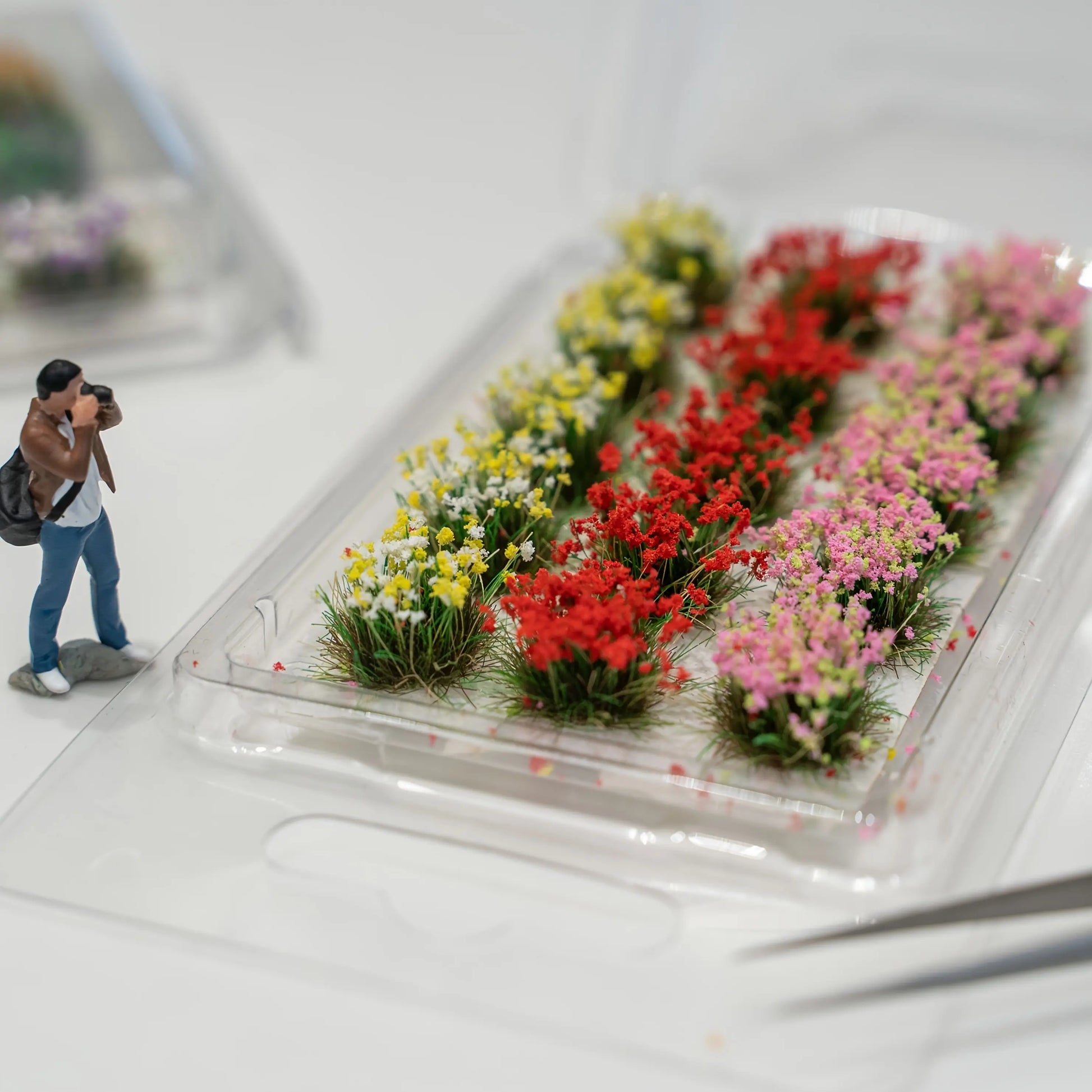 Pink mixed tiny flower tuft held by tweezers, pre-glued backing easy to apply on dollhouse and model scenes
