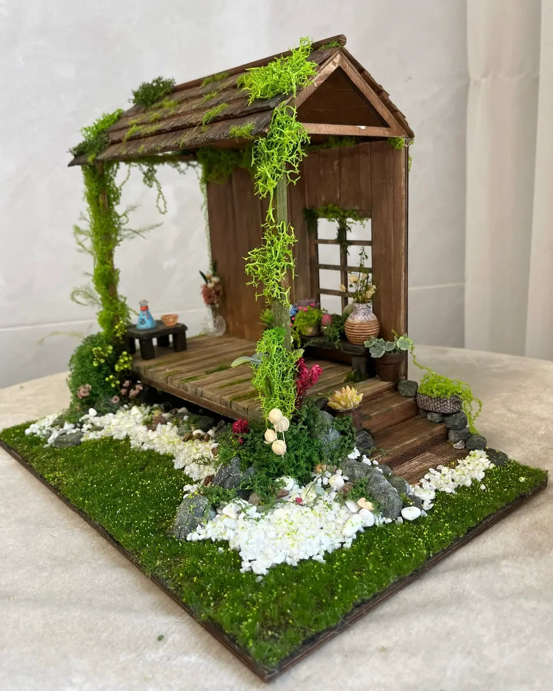 Static grass tufts decorating a miniature garden house diorama with realistic landscaping, flowers and moss details