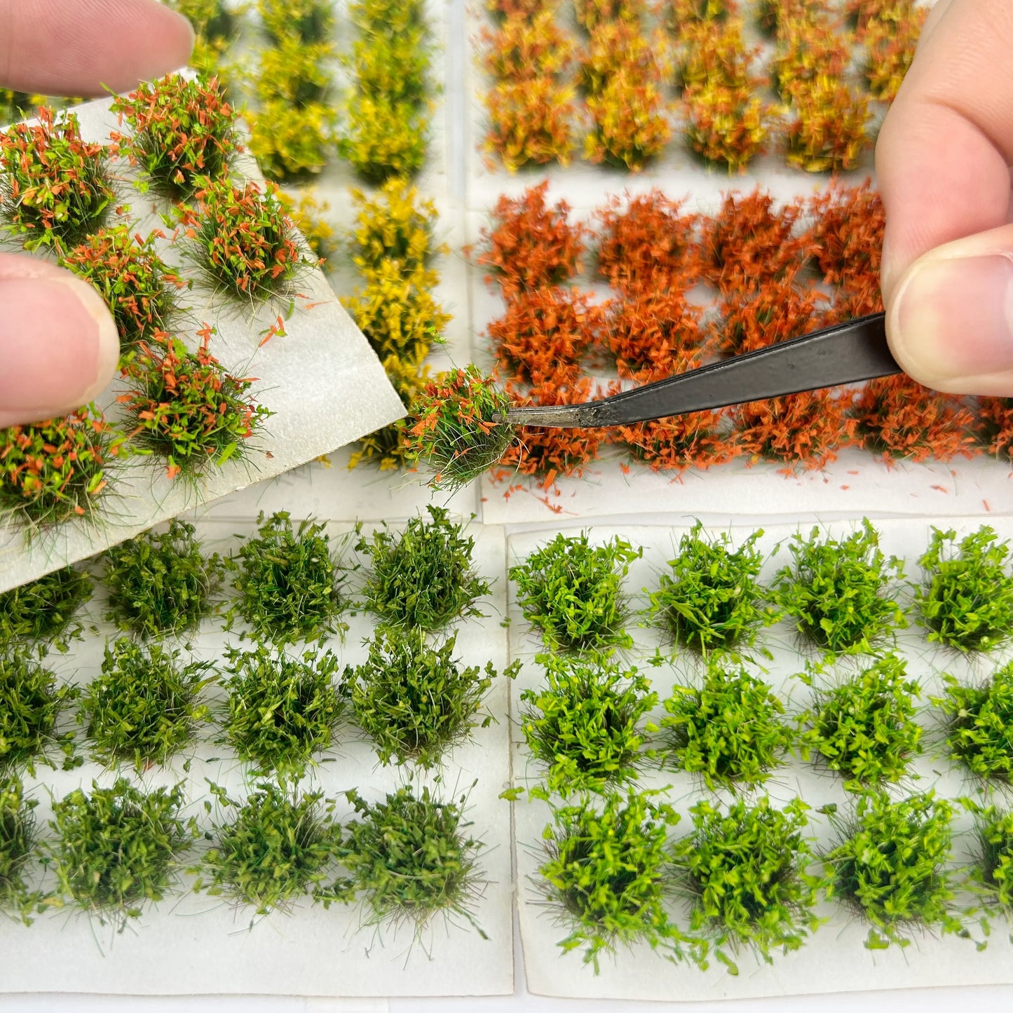 Multi tone miniature static grass tuft display with tweezers picking grass clump, assorted seasonal grass sheets for DIY diorama terrain and wargame base building