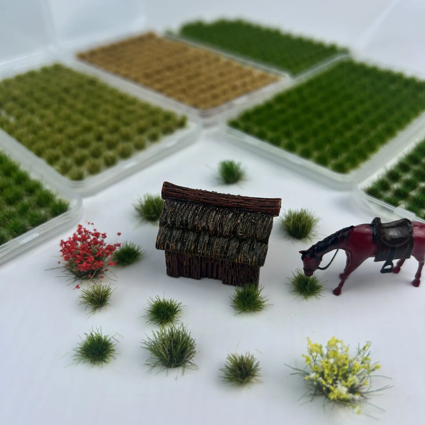 Combination display of multi-color self-adhesive static grass tufts sheets with miniature thatched hut, horse model and flower clusters, versatile terrain material demo for diorama creators, static grass tufts, miniature diorama supplies, wargame terrain material, model railway grass, self-adhesive grass clusters, scale model scenery, warhammer terrain, hobby craft grass