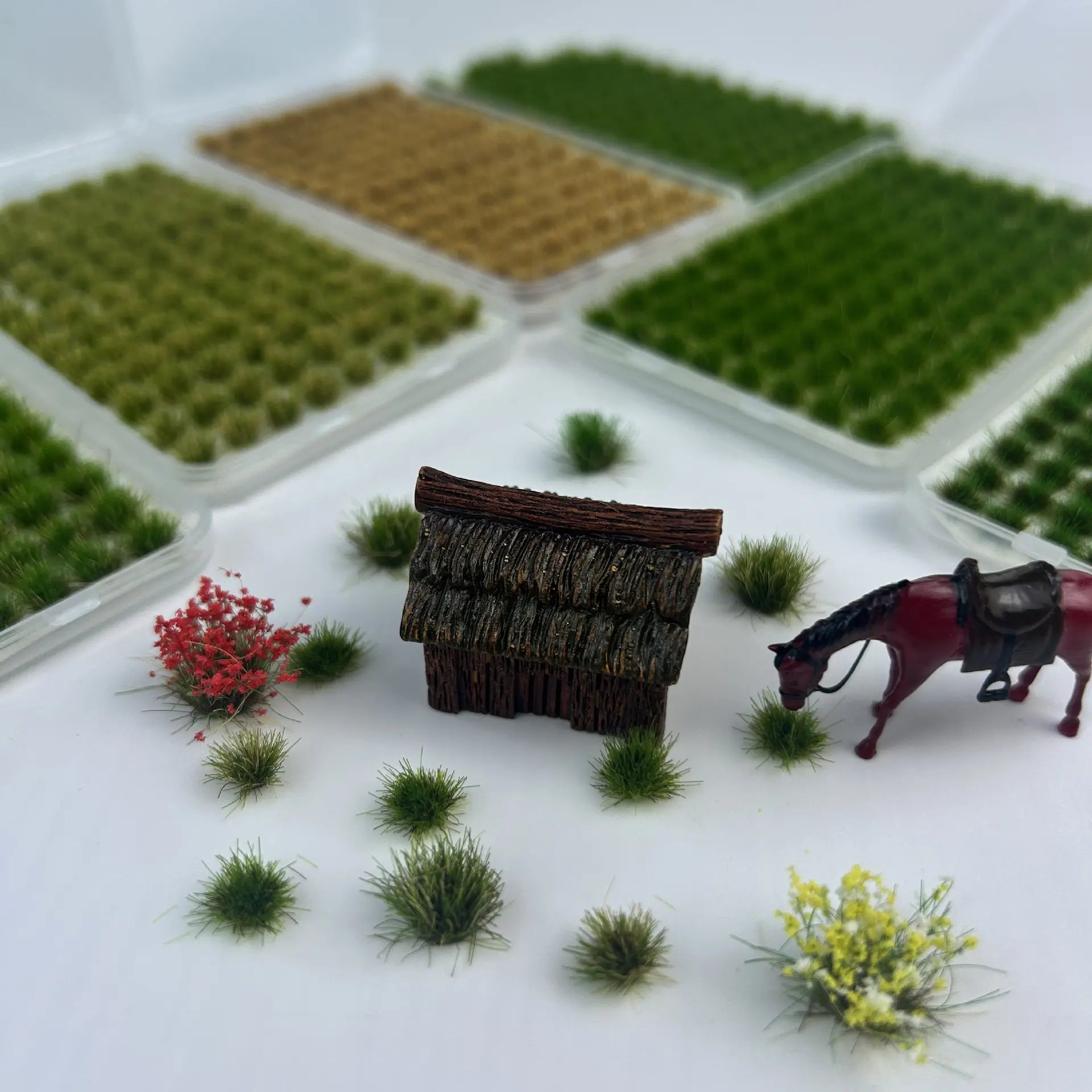 Combination display of multi-color self-adhesive static grass tufts sheets with miniature thatched hut, horse model and flower clusters, versatile terrain material demo for diorama creators, static grass tufts, miniature diorama supplies, wargame terrain material, model railway grass, self-adhesive grass clusters, scale model scenery, warhammer terrain, hobby craft grass