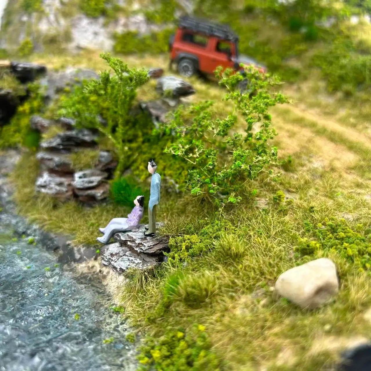 Natural riverside mountain miniature terrain diorama set with couple tiny people figures, realistic static grass, rock and bush scenery for landscape scale model, wargame and handmade diorama craft
