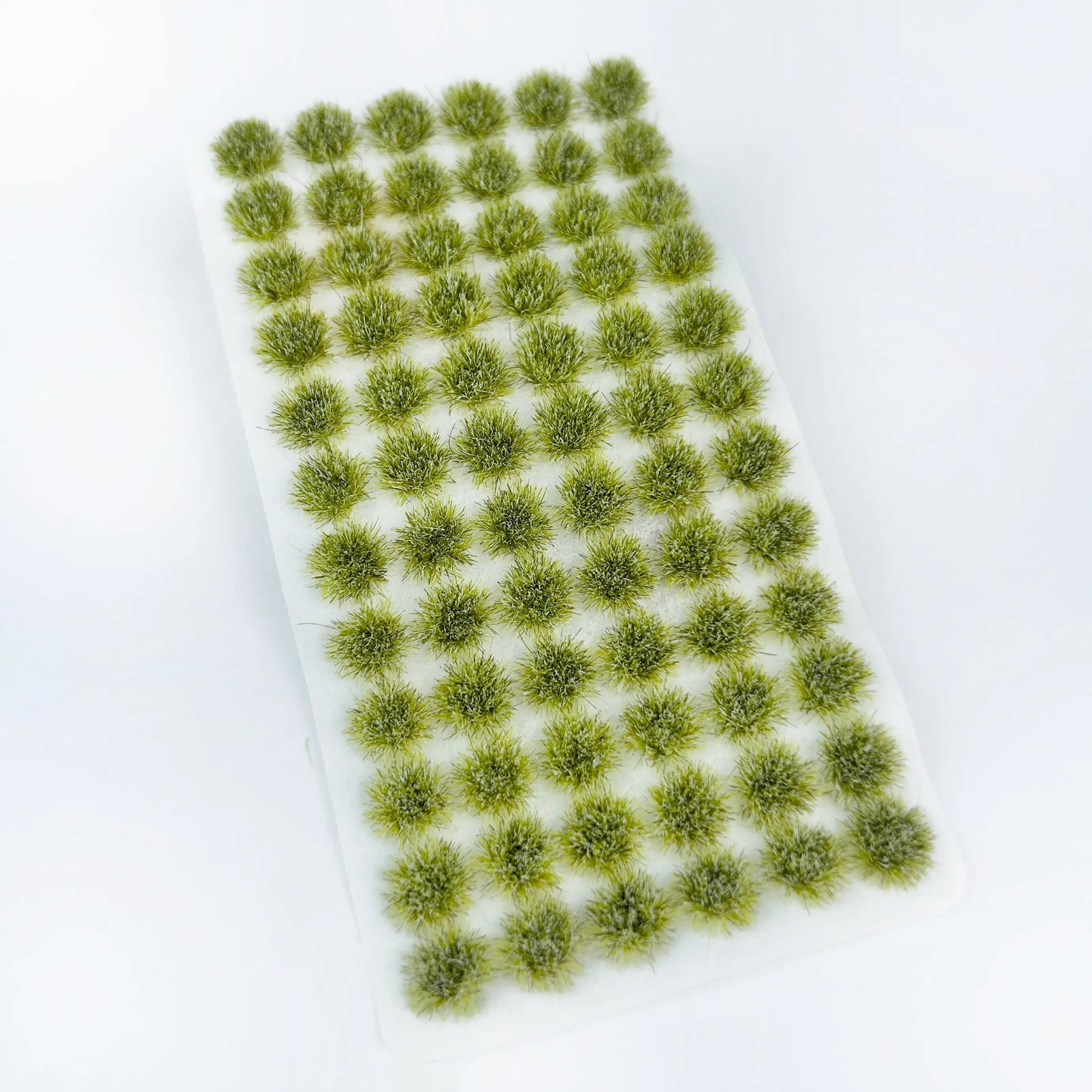 Unpacked sheet of pale yellow-green spring static grass tufts on solid white background, soft light tone grass clumps for meadow, farm and early spring miniature scene terrain