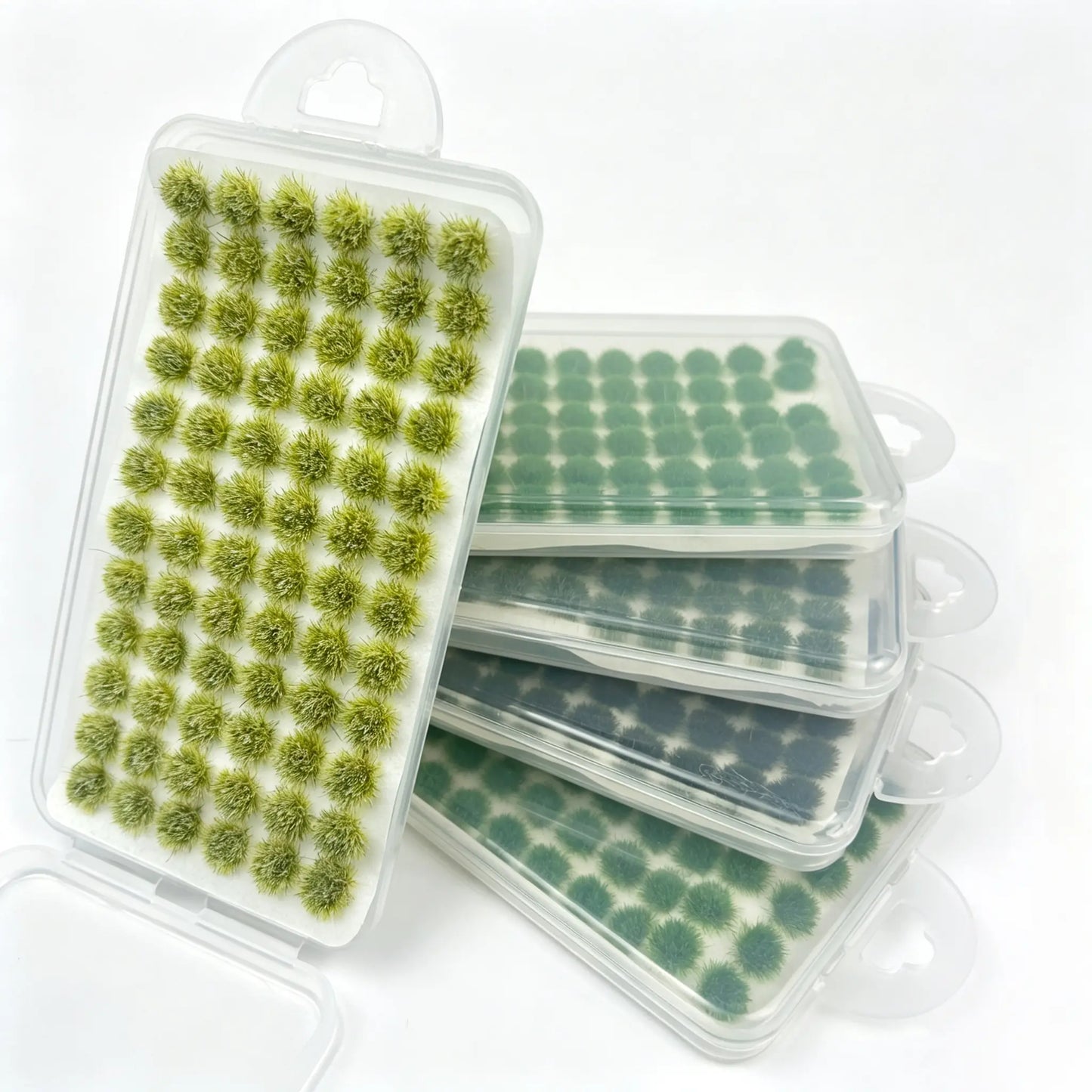 Open hanging plastic blister packs stacked together, assorted spring light yellow-green gradient self-adhesive static grass tufts, multi-shade green set display for miniature farm diorama, model railway and tabletop wargame terrain landscaping supplies