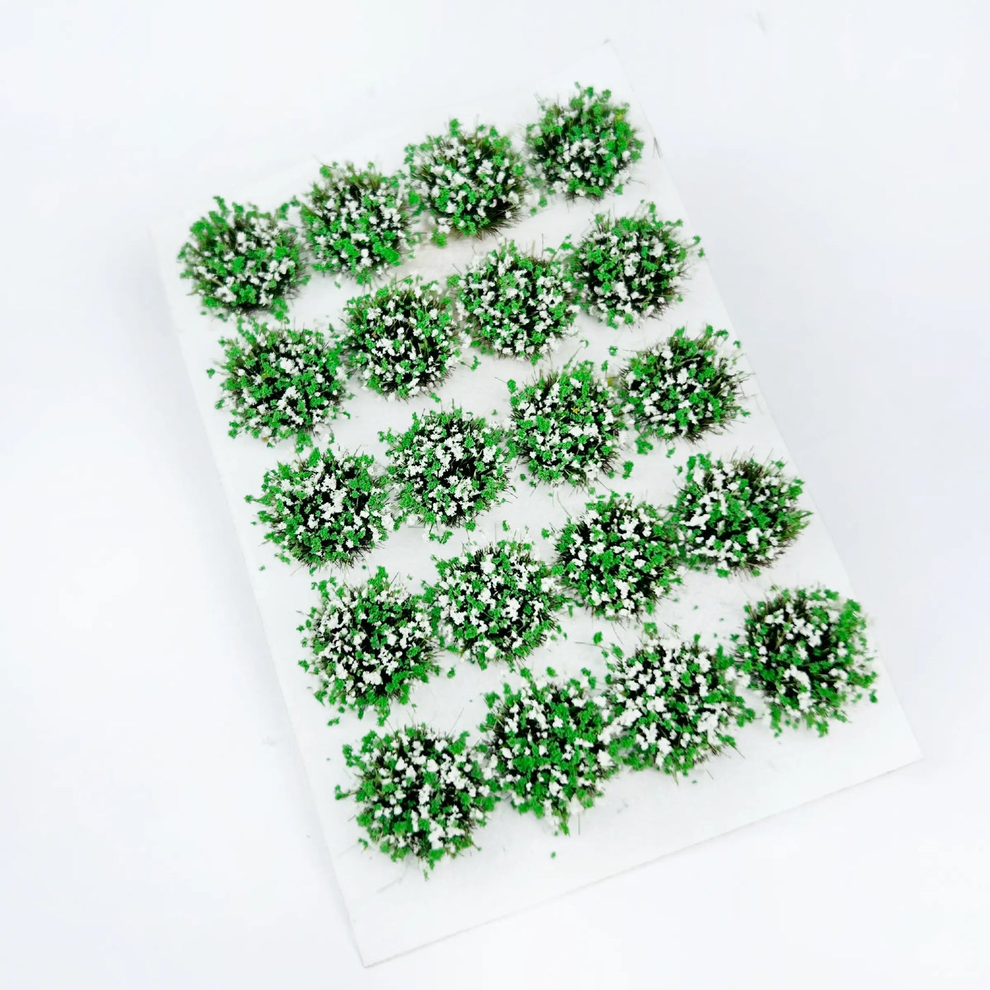 Lush fresh green self-stick round static grass tuft sheet dotted with tiny white wildflower clusters, spring mini foliage clumps for woodland garden diorama layout, tabletop wargame terrain and scale railway model landscaping supplies