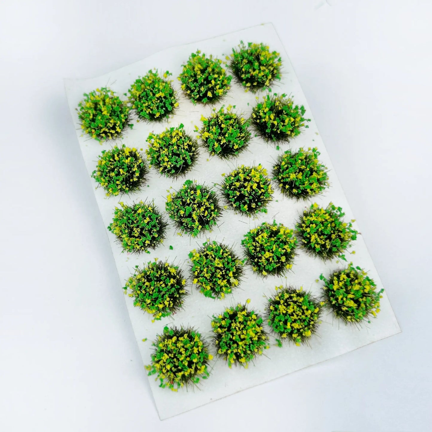 Soft light green round self-stick static grass tuft sheet filled with delicate yellow wildflower clusters, spring meadow mini grass clumps for countryside diorama layout, sci-fi & historical wargame terrain and scale train model scenery
